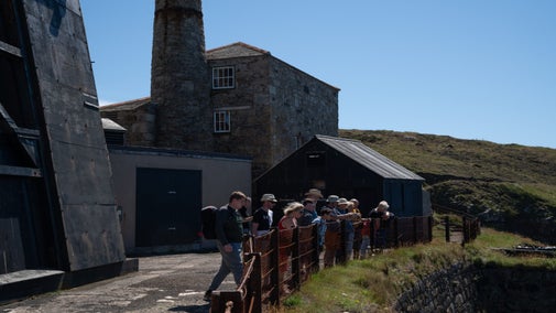 A group of people being given a tour by the zawn at Levant Mine and Beam Engine, Cornwall.